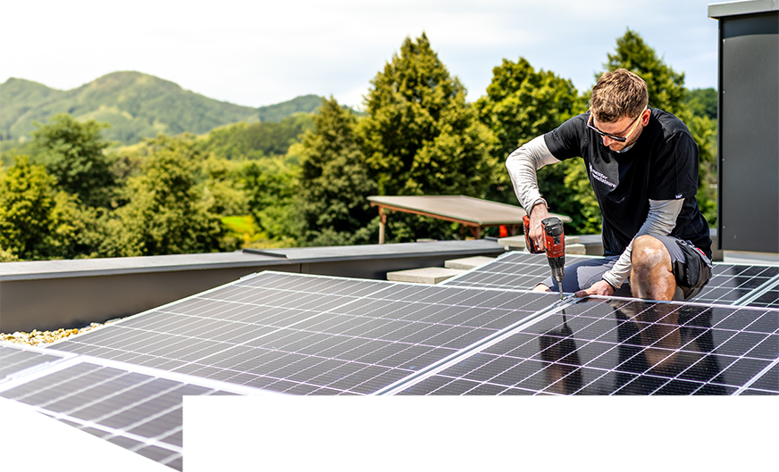 Installateur mit Bohrmaschine in der Hand montiert eine Photovoltaikanlage auf einem Hausdach.