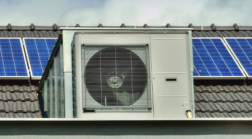 Wärmepumpen-Außengerät vor einer Photovoltaikanlage, beides auf einem Hausdach.