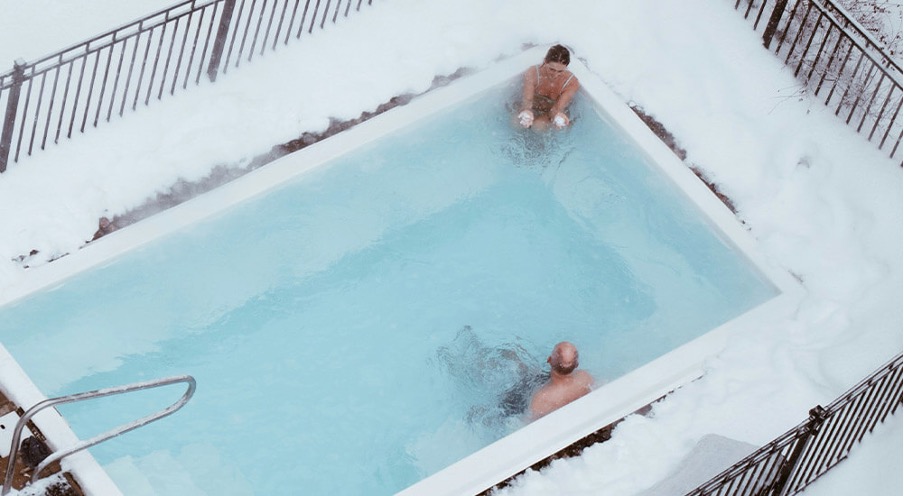 Großer, beheizter Out-door-Swimmingpool in Winterlandschaft mit zwei Personen drinnen.